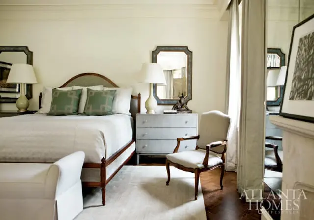 Bedroom with a queen-size bed, green patterned pillows, a light gray dresser with a lamp, and an upholstered armchair.