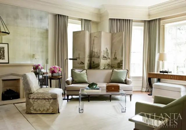 Living room with a neutral sofa, patterned armchair, and a folding screen depicting sailing ships. A clear acrylic coffee table sits in front of the sofa.