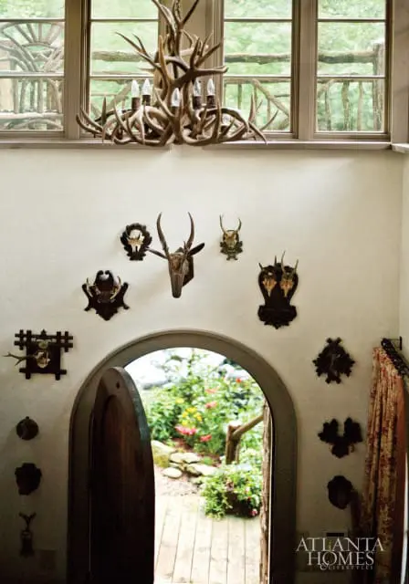 Hallway with a large antler chandelier, mounted animal skulls and antlers on the wall, and an arched doorway opening to a garden