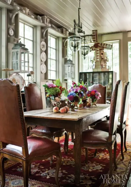Rustic wooden dining table with leather chairs, floral arrangements, and peaches, set on a patterned rug.