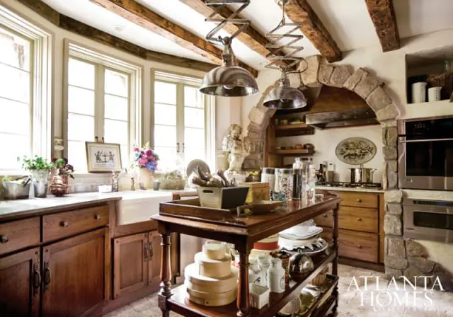 Rustic kitchen with exposed wooden beams, stone archway over range, farmhouse sink, and wooden island