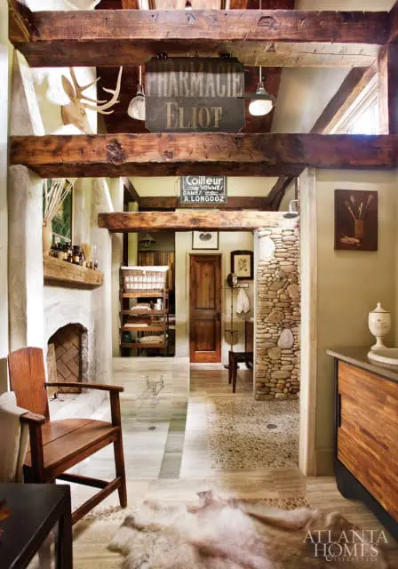 Rustic bathroom with exposed wooden beams, stone shower, fireplace, wooden chair, and a sheepskin rug.