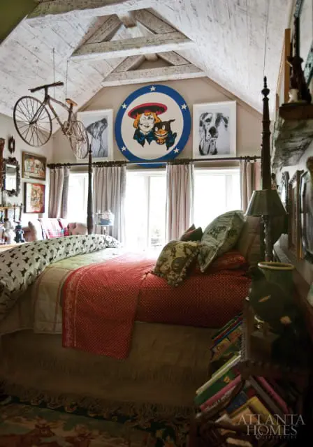 Bedroom with a pitched, white-washed wood ceiling, a hanging bicycle, and a bed with red and patterned bedding.