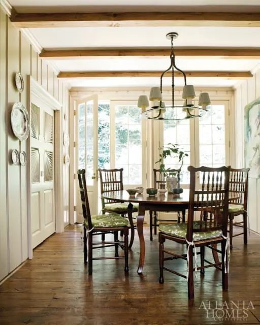 Dining room with dark wood table and chairs with green patterned cushions, exposed wood beams on ceiling, and paneled walls.
