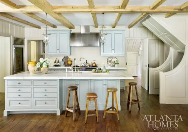 Light blue kitchen island with marble countertop, white paneled walls, exposed wood beams, and stainless steel appliances.