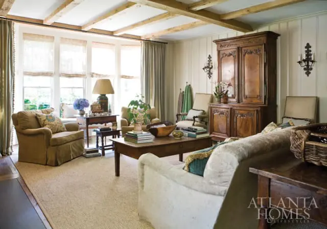 Living room with exposed wooden beams on the ceiling, a large wooden armoire, upholstered armchairs, a coffee table with books, and a sectional sofa.