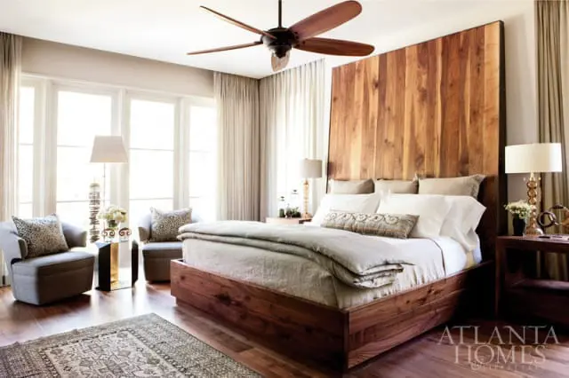 Bedroom with a large wooden headboard, wooden platform bed, two upholstered chairs with leopard print pillows, and a patterned rug.