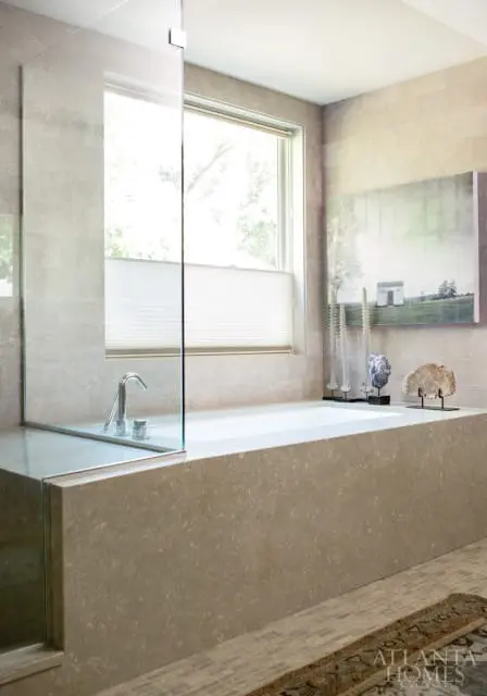 Modern bathroom with a freestanding soaking tub, glass shower enclosure, stone tile walls, and a minimalist landscape painting above the tub.
