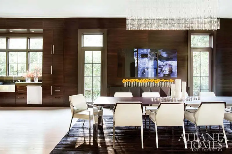 Dining room with dark wood paneled walls, white upholstered chairs around a dark wood table, and a modern chandelier.