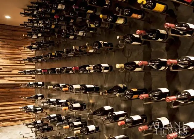 Modern wine cellar with dark wood paneled wall and floor-to-ceiling metal wine racks filled with bottles.