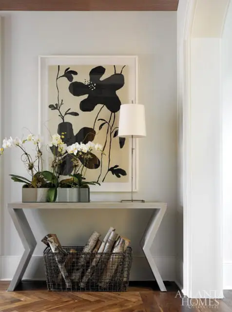 Entryway console table with orchids, a modern floral art print, and a basket of firewood below.