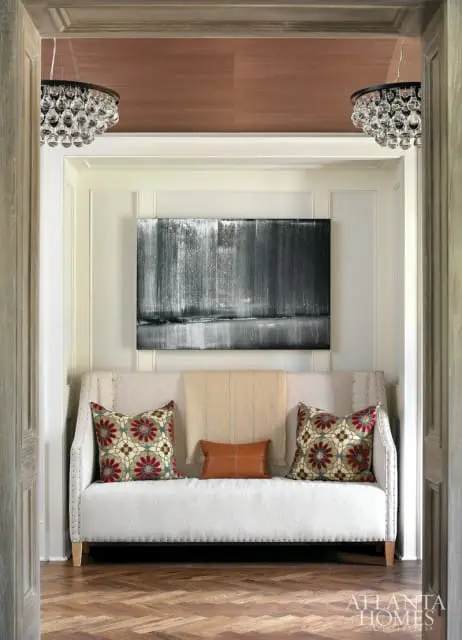 Hallway with a cream upholstered sofa, abstract art, crystal chandeliers, and herringbone wood floors.
