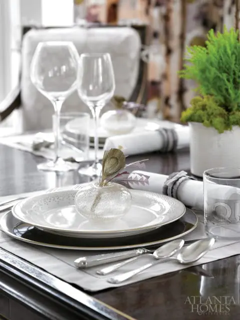 Close-up of a formal place setting with white plates, silver cutlery, wine glasses, and a small glass vase with a feather