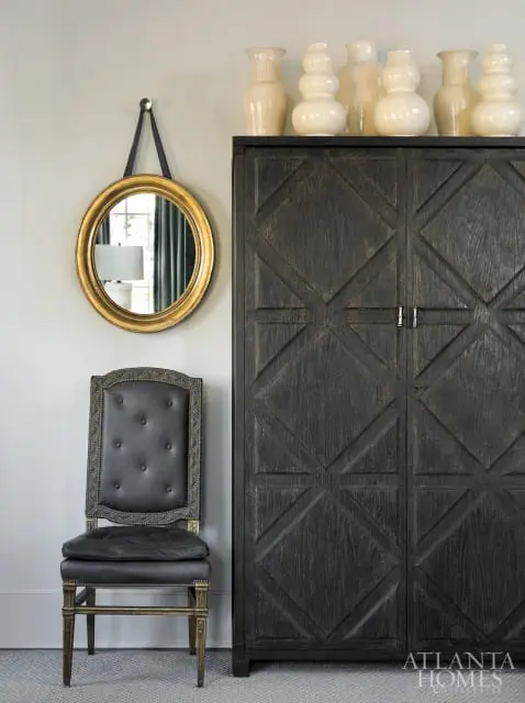 Dark wood cabinet with geometric pattern, gold framed mirror, and tufted leather chair with nailhead trim.