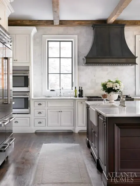 Luxury kitchen with white marble backsplash, dark metal range hood, white cabinetry, and a dark wood island with a farmhouse sink.