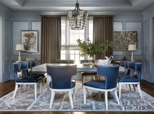 Dining room with blue leather chairs featuring silver nailhead trim around a light gray dining table, under a glass orb chandelier.