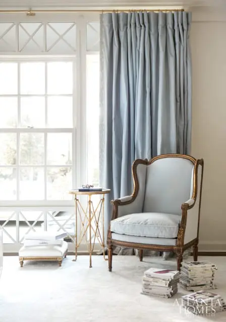 Light blue armchair with gold trim next to a small gold accent table and a stack of magazines on a light gray rug.
