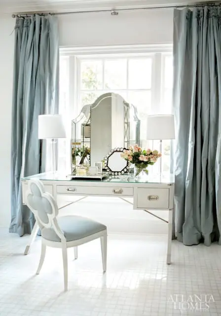 White vanity desk with a glass top, silver hardware, and a scalloped clover-shaped chair in a light blue upholstered seat.