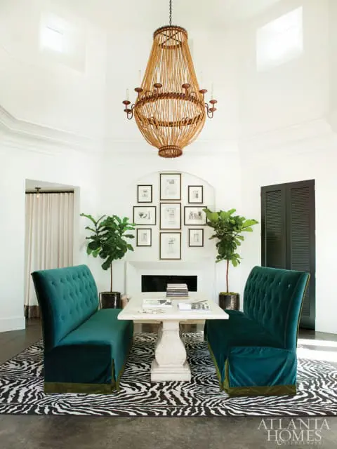 Dining area with two teal velvet tufted banquettes, a stone pedestal table, a large rope chandelier, and a zebra print rug.