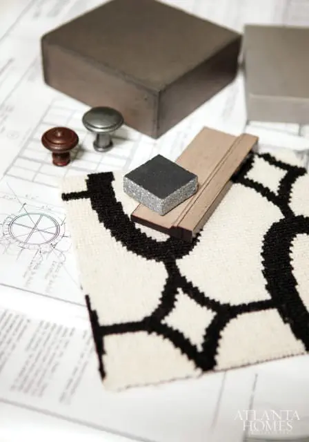 Material samples including wood trim, metal knobs, stone tile, and fabric swatch with black and white geometric pattern, laid over architectural blueprints.