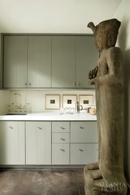 Sage green kitchen cabinetry with silver hardware, white quartz countertop, stainless steel faucet, and a large stone Buddha statue.