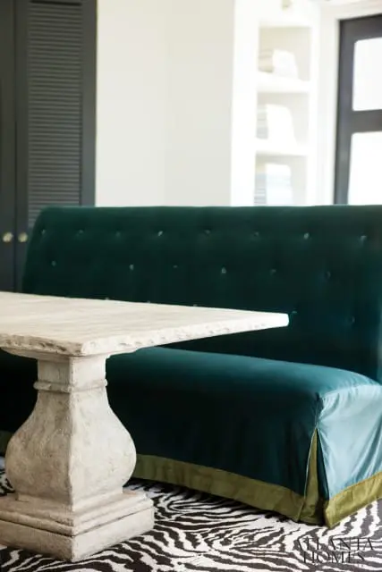 Dining area with a tufted teal velvet banquette, a stone pedestal table, and a zebra print rug.
