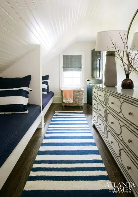 Attic bedroom with white beadboard ceiling, navy and white striped runner, built-in twin beds with navy bedding, and a decorative dresser.