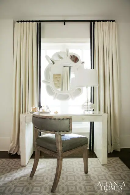 Dressing table with a white bone inlay finish, a glass lamp, and a decorative mirror above. A grey upholstered chair with nailhead trim sits in front of the table.