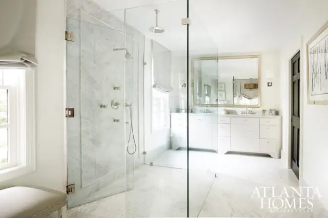 Spacious white bathroom with a large marble shower enclosure, double vanity with white cabinetry, and marble tile flooring.