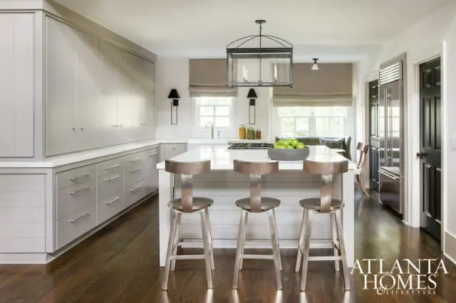 Gray kitchen with white quartz island, stainless steel stools, floor-to-ceiling gray cabinetry, and dark wood floors.