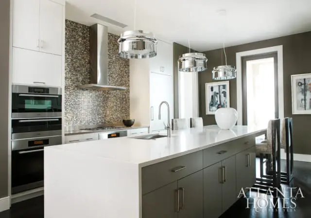 Modern kitchen with white quartz island, gray cabinetry, stainless steel appliances, and mosaic tile backsplash. Three chrome pendant lights hang above the island.