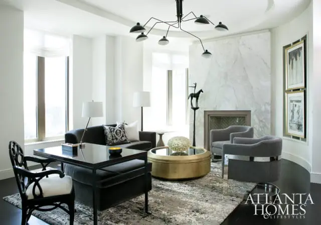 Modern living room with dark gray sofa, black desk, gold coffee table, marble fireplace, and abstract rug.