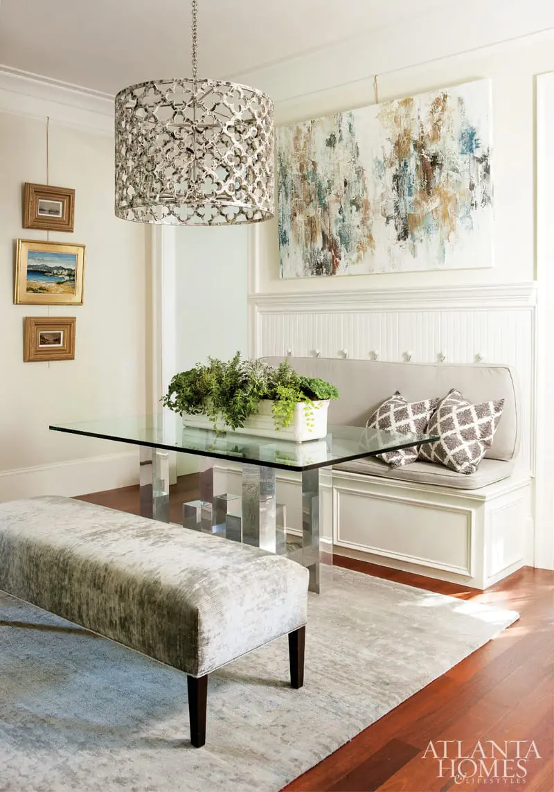 Dining area with glass-top table on acrylic block legs, upholstered bench seating, and a plush bench on a textured rug.