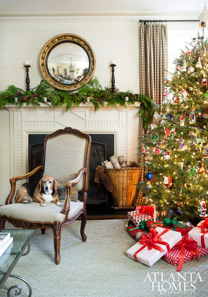 Living room with a fireplace decorated for Christmas, a beagle dog resting on an antique chair, and a decorated Christmas tree with presents underneath.