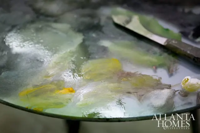 Close-up of an artist's palette with dabs of yellow, green, and white oil paint, and a palette knife resting on the surface.