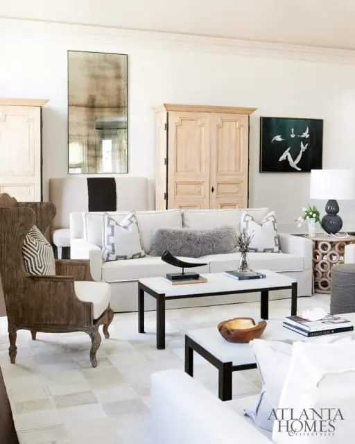 Living room with a white sofa, wooden armchairs, a large distressed mirror, and two-tiered coffee table.