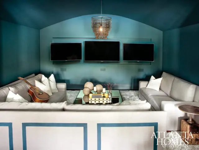 Living room with teal walls and ceiling, three mounted televisions, sectional sofas, and a guitar on a sofa.