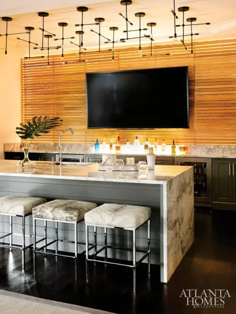 Bar area with marble island, furry stools, wood slat wall, and a large television.