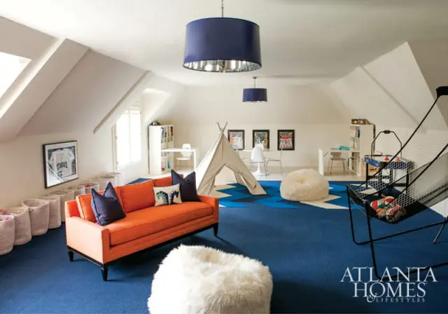 Attic playroom with an orange sofa, white teepee, blue and white geometric rug, and basketball hoop game.