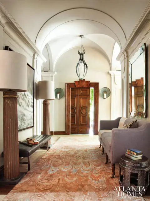 Entryway with vaulted ceiling, double wooden doors, a gray sofa, a leather bench, and a large rug with an abstract pattern.