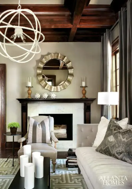 Living room with a dark wood beamed ceiling, marble fireplace, and upholstered furniture. A large, ornate mirror hangs above the fireplace.
