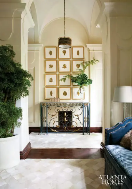 Hallway with arched ceiling, featuring a grid of framed botanical prints, a dark metal console table with ornate gold accents, and a large potted plant.