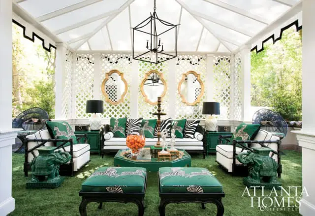 Sunroom with white lattice walls, black lantern chandelier, and white seating with green and zebra-print cushions. Green elephant garden stools flank the seating area.