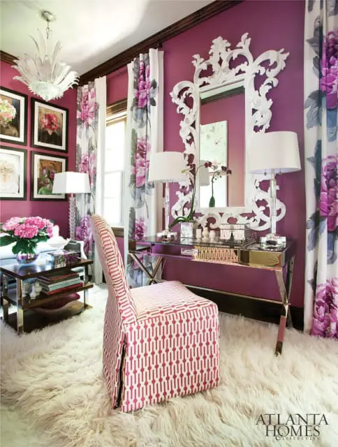 Purple room with a white ornate mirror, glass desk, floral curtains, and a pink patterned chair on a cream shag rug.