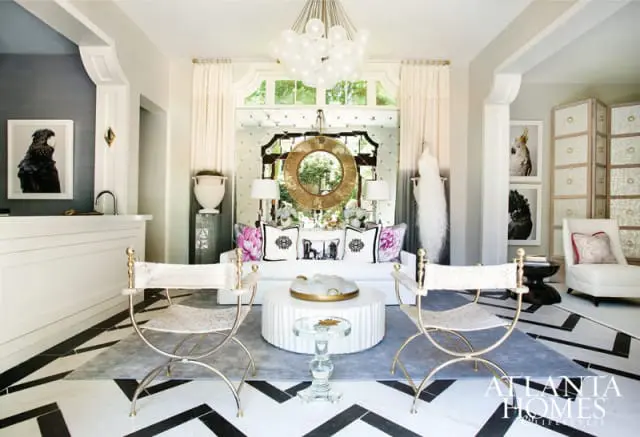 Living room with black and white geometric floor, white sofa with floral and patterned pillows, gold-framed mirror, and a large white chandelier.