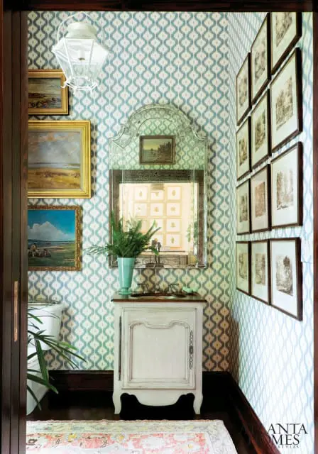 Powder room with blue and white ikat wallpaper, a white vanity with a dark wood countertop, a vintage mirror, and framed artwork on the walls.