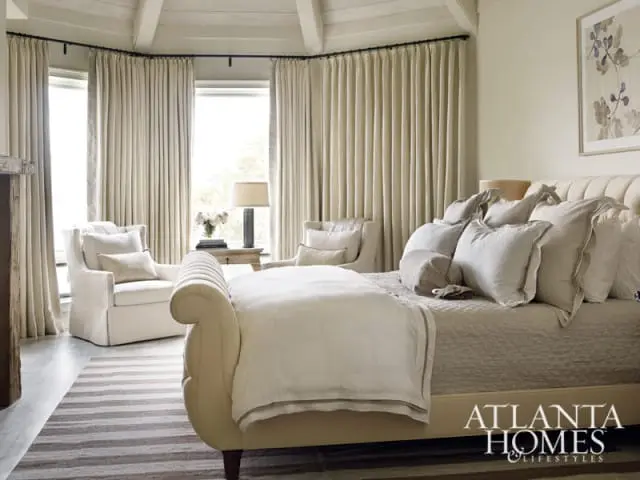 Bedroom with a tufted headboard bed, upholstered chairs, and floor-to-ceiling curtains. The Atlanta Homes & Lifestyles logo is visible in the lower right corner.