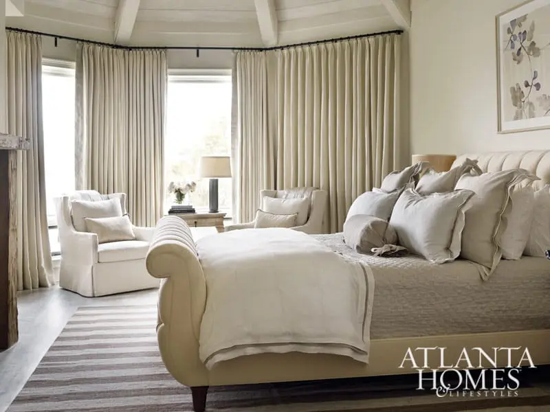 Bedroom with a tufted headboard bed, upholstered chairs, and floor-to-ceiling curtains. The Atlanta Homes & Lifestyles logo is visible in the lower right corner.