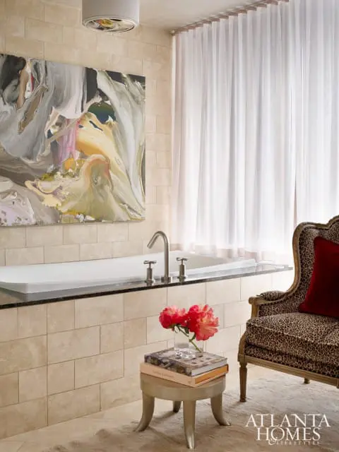 Bathroom with a freestanding tub, abstract art, sheer curtains, and a leopard-print armchair with a red pillow.