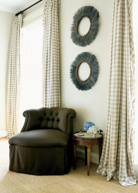 Dark brown tufted slipper chair next to a small wooden side table with hydrangeas and two circular wall hangings with fringe above